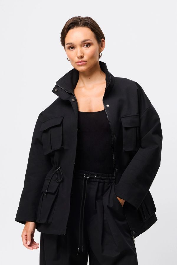 Mossman My Muse Anorak in Black, a modern utility jacket featuring oversized flap pockets, adjustable drawstring waist, and a concealed zip front for an elevated off-duty look. 4 