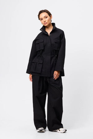 Mossman My Muse Anorak in Black, a modern utility jacket featuring oversized flap pockets, adjustable drawstring waist, and a concealed zip front for an elevated off-duty look.