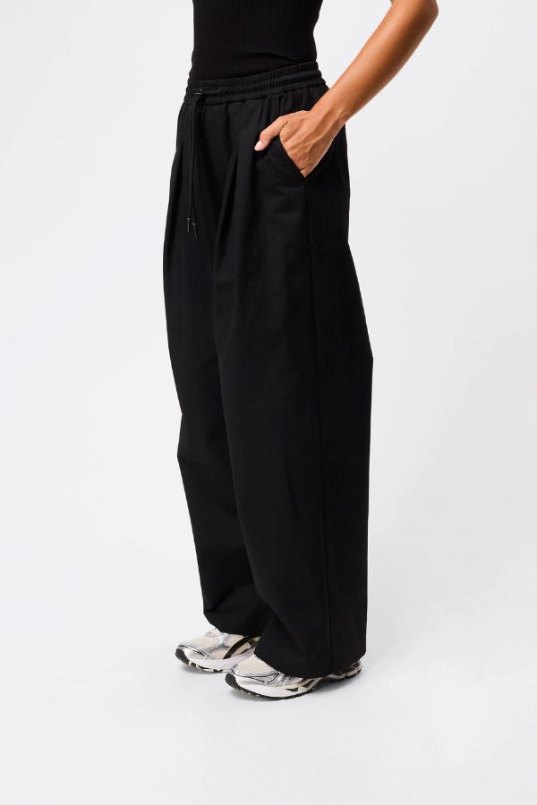 Mossman Tied Down Pant in Black, a wide-leg cotton pant featuring an elasticated waistband with adjustable toggle and functional pockets for chic utility style.
