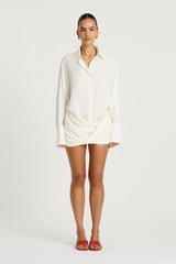 Riya Shirt Dress in White by Benni, a cotton mini shirt dress with oversized sleeves, button front, and twist skirt detail.