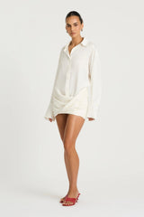 Riya Shirt Dress in White by Benni, a cotton mini shirt dress with oversized sleeves, button front, and twist skirt detail.