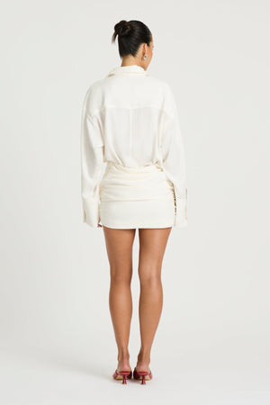 Riya Shirt Dress in White by Benni, a cotton mini shirt dress with oversized sleeves, button front, and twist skirt detail.