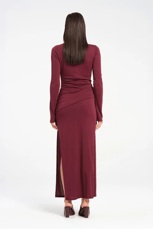 Sacha Mini Dress in Plum by Benni, crafted from stretch jersey with a high neckline, long sleeves, and angled chest cut-out. Draped waist sash and gathered skirt for dynamic texture.
