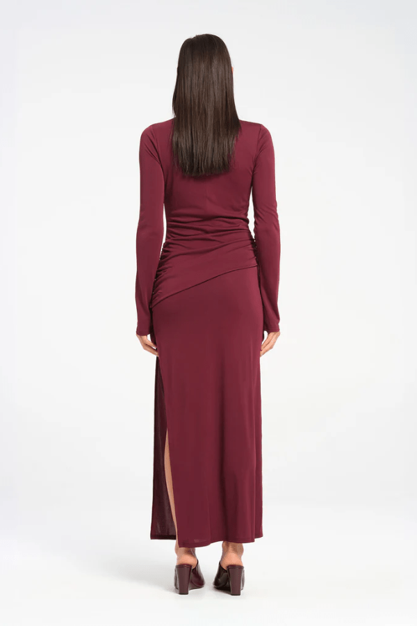 Sacha Mini Dress in Plum by Benni, crafted from stretch jersey with a high neckline, long sleeves, and angled chest cut-out. Draped waist sash and gathered skirt for dynamic texture.