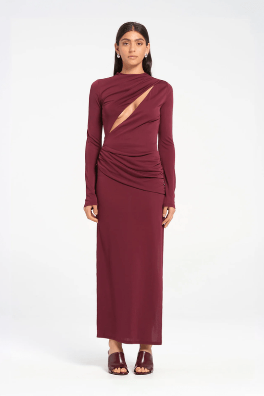 Sacha Mini Dress in Plum by Benni, crafted from stretch jersey with a high neckline, long sleeves, and angled chest cut-out. Draped waist sash and gathered skirt for dynamic texture.