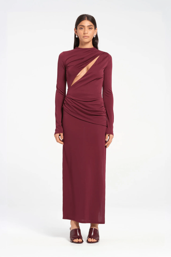 Sacha Mini Dress in Plum by Benni, crafted from stretch jersey with a high neckline, long sleeves, and angled chest cut-out. Draped waist sash and gathered skirt for dynamic texture.