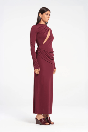 Sacha Mini Dress in Plum by Benni, crafted from stretch jersey with a high neckline, long sleeves, and angled chest cut-out. Draped waist sash and gathered skirt for dynamic texture.