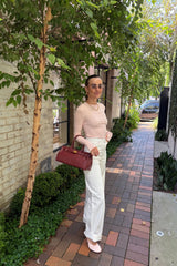 The Polly Long Sleeve top in pink. Woman in a pink top and white pants standing outside a store with plants and a bench in the background.