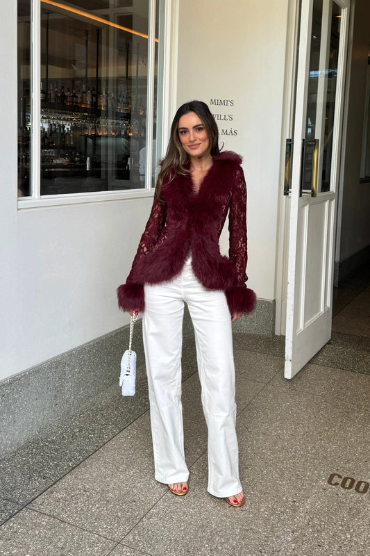 A young woman wears a burgundy lace top with thick faux fur trim on collar and cuffs, paired with blue jeans and gold aviator glasses.