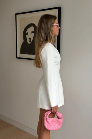 A young woman in a white Bobbie Long Sleeve Mini Dress poses with a bright pink woven leather handbag against a minimalist backdrop.