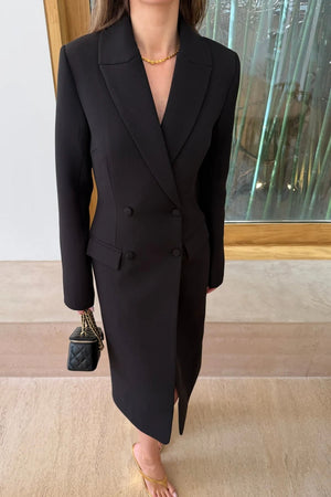 A woman wears the Carissa Tailored Midi Dress Black with gold sandals and a quilted black bag in a minimalist space with bamboo visible outside.
