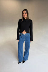 A woman wears the Charlotte Cropped Blazer Top Black with high-waisted blue jeans and black patent heels against a grey backdrop.