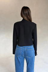 Woman seen from behind wearing a black Charlotte Cropped Blazer Top paired with mid-wash blue jeans against a neutral background.