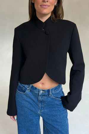 Woman wearing a black Charlotte Cropped Blazer Top with curved hem and blue high-rise jeans against a neutral background.
