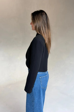 A young woman in profile wears a structured black Charlotte Cropped Blazer Top paired with classic blue denim jeans.