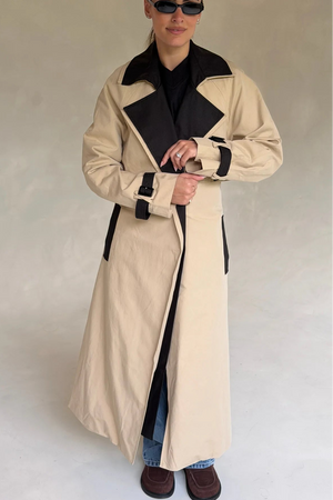 Beige Dakota trench coat with black contrast details, featuring a belted waist and classic collar.