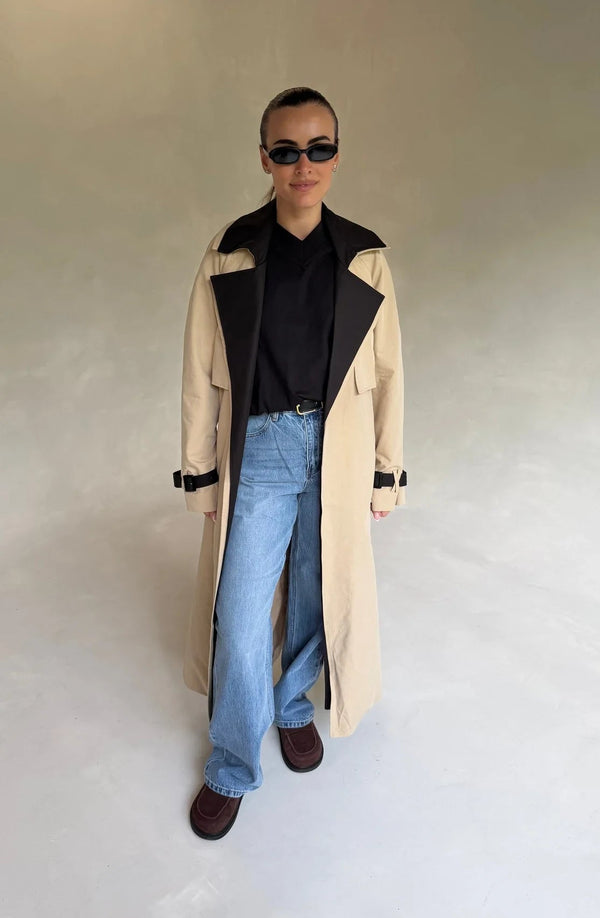 Beige Dakota trench coat with black contrast panels, featuring a belted waist and classic collar.