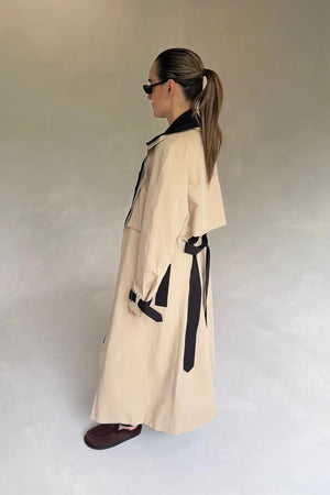 Beige Dakota trench coat with black contrast panels, featuring a belted waist and classic collar.