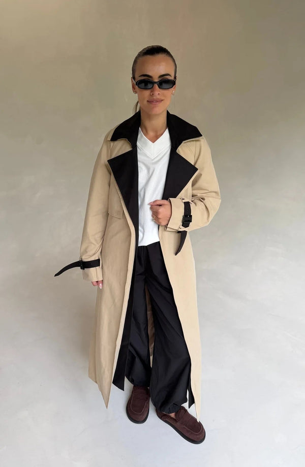 Beige Dakota trench coat with black contrast panels, featuring a belted waist and classic collar.