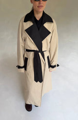 Beige Dakota trench coat with black contrast detailing, featuring a belted waist and classic collar.