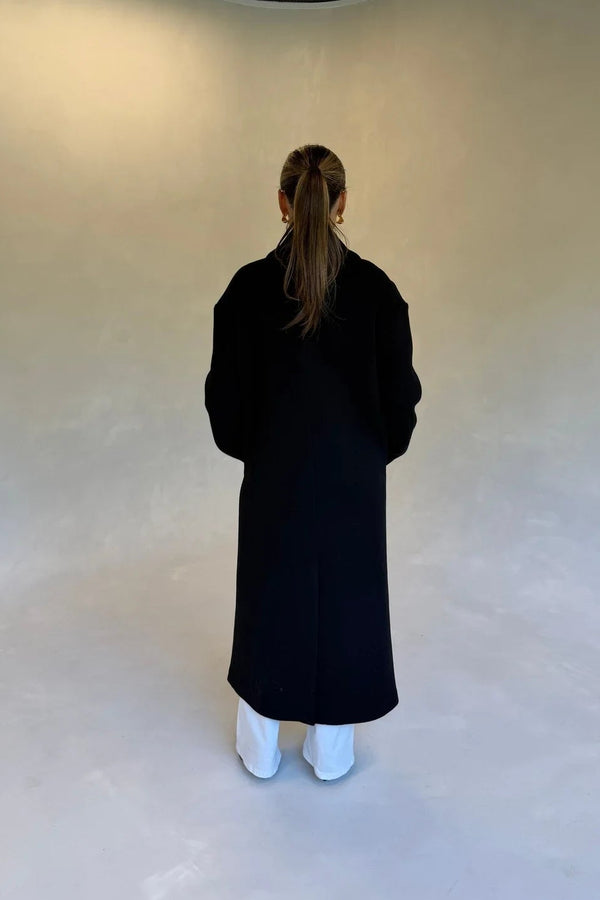 Black double-breasted coat with wide lapels and button details, designed for a tailored fit.