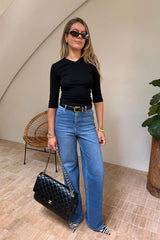 A woman wears the Esme High V black 3/4 sleeve top paired with wide-leg jeans and zebra-print heels in a bright, minimalist room.