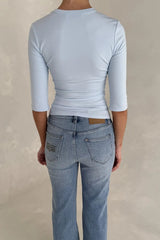 Woman wearing an Esme High V 3/4 Sleeve Top in light blue paired with light-wash Sneaky Link jeans, shown from behind.