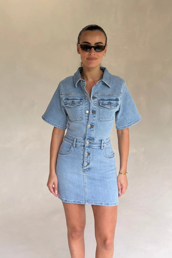 Light blue denim mini dress with short sleeves and a fitted silhouette, styled with front buttons and a casual look.