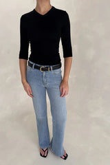 A woman wears Kendall Mid Rise Flare Jeans in mid wash paired with a fitted black v-neck top, black belt, and square-toe sandals.