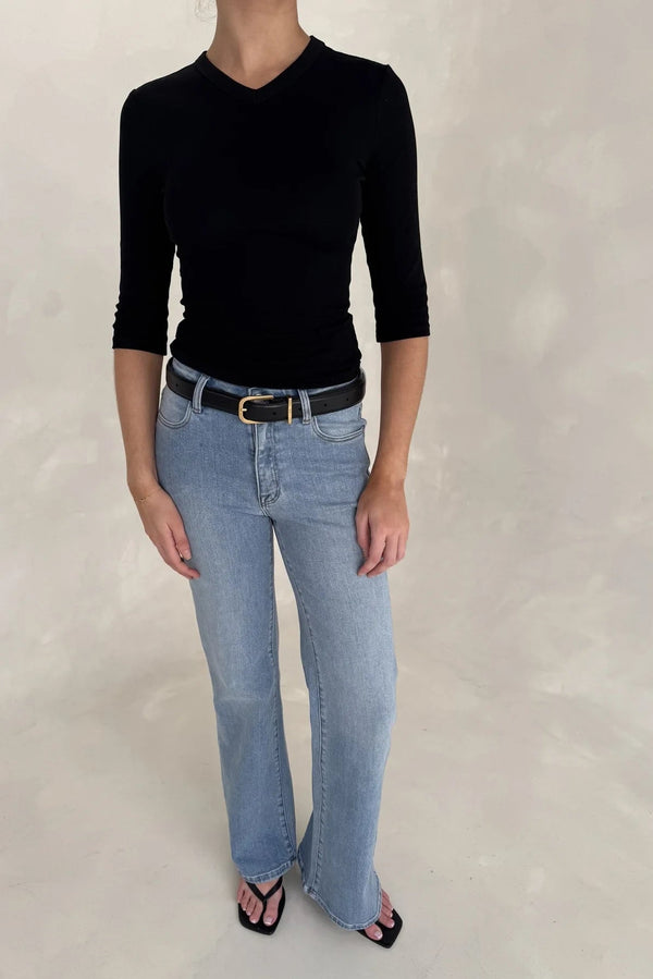 A woman wears Kendall Mid Rise Flare Jeans in mid wash paired with a fitted black v-neck top, black belt, and square-toe sandals.