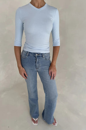 A woman wears Kendall Mid Rise Flare Jeans in mid wash paired with a light blue ribbed top and white square-toe wedge sandals.