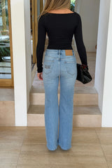 A woman wears Kendall Mid Rise Flare Jeans in mid wash with a black long-sleeve top and a black crocodile-textured handbag.