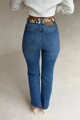 Woman wearing high-waisted Kennedy Crop Jean Indigo with a snakeskin belt, white long-sleeve top, and white stiletto heels.