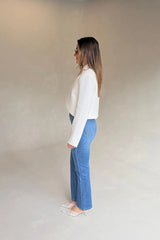 A woman in profile wears Kennedy Crop Jean Indigo with a white blazer and lace kitten heels against a minimalist beige and grey studio backdrop.