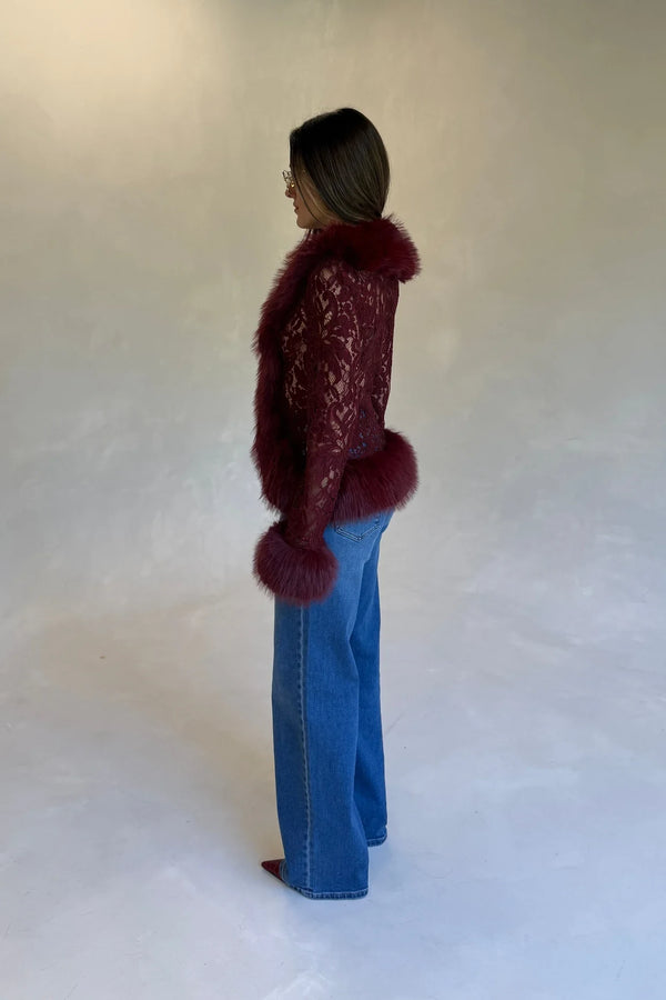 A woman in a burgundy Lace Fur Trim Top with faux fur collar and cuffs, paired with medium-wash jeans and pointed-toe shoes.