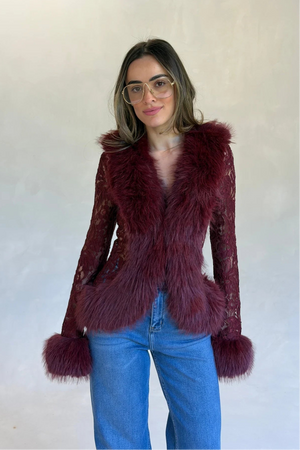 A young woman wears a burgundy lace top with thick faux fur trim on collar and cuffs, paired with blue jeans and gold aviator glasses.