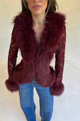 A woman wears a burgundy lace fur trim top with thick faux fur collar and cuffs, paired with blue jeans and pointed heels.
