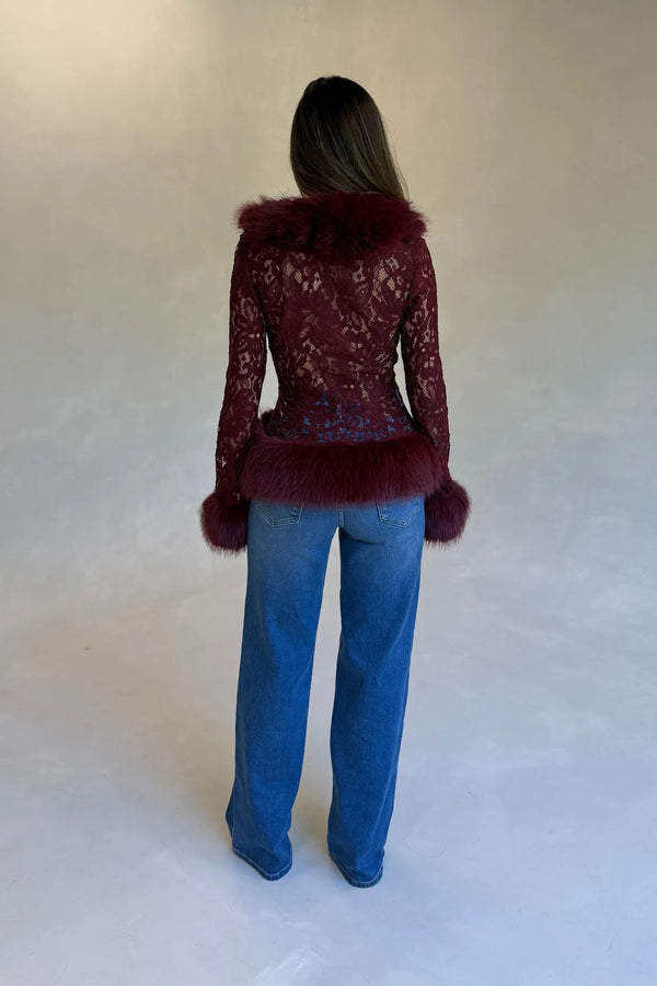 Model wearing a burgundy lace fur trim top with plush faux fur at collar, cuffs, and hem, paired with medium-wash blue jeans.