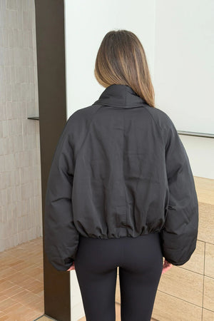 Person wearing a black Maddison Shawl Collar Oversized Jacket with cropped elastic hem and matching black leggings, seen from behind.