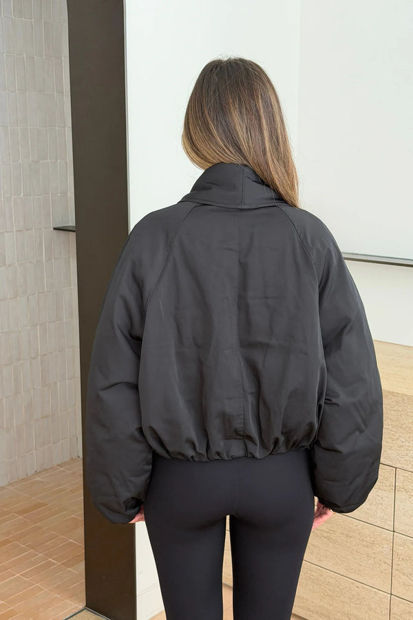 Person wearing a black Maddison Shawl Collar Oversized Jacket with cropped elastic hem and matching black leggings, seen from behind.