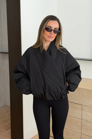 A young woman wears a black Maddison Shawl Collar Oversized Jacket with fitted leggings and dark oval Gucci sunglasses in a minimalist setting.