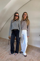 Two women pose in a bright, minimalist room wearing Millie Relaxed Long Sleeve Tees in black/white and brown/white stripes.