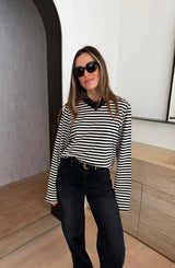 A woman wears a Millie Relaxed Long Sleeve Tee in black and white stripes with black jeans and dark-framed sunglasses in a minimalist interior.