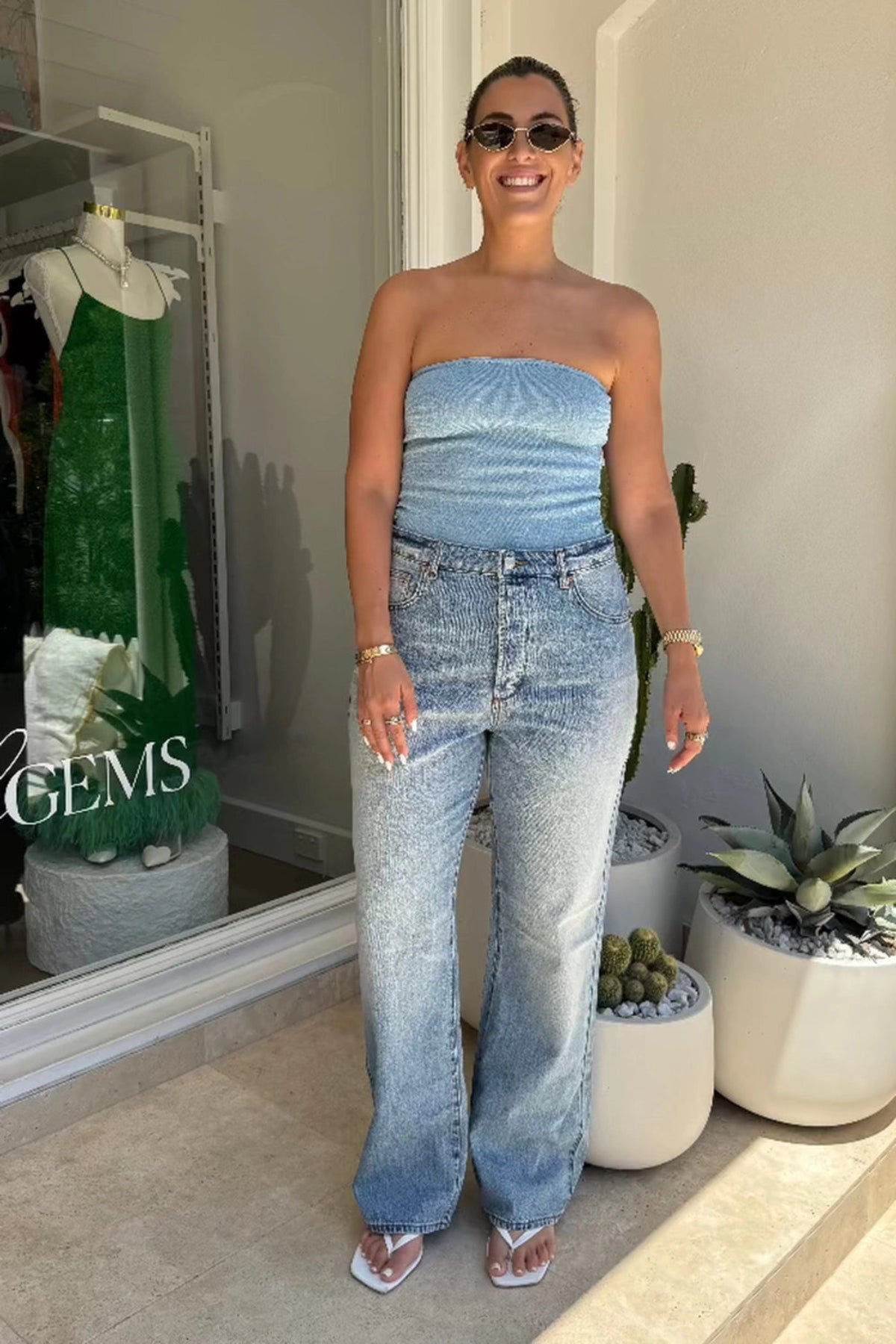 Woman wearing a denim strapless top and jeans standing in front of a mirror.