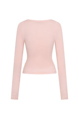 The Polly Long Sleeve top in pink. Woman in a pink top and white pants standing outside a store with plants and a bench in the background.