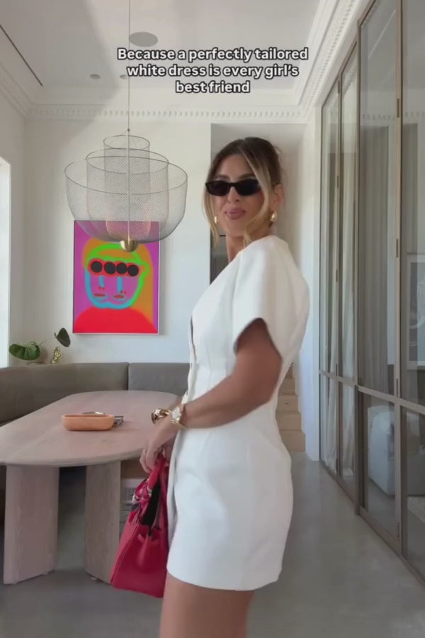 Sophia Mini Dress White by Sneaky Link – Chic and structured with short sleeves, deep V-neck, and contrast black buttons. Crafted from a luxe cotton-nylon blend for a flattering hourglass fit. Perfect for any occasion. Cold wash, line dry. Size down if in between.