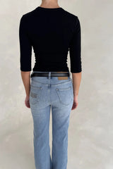 Rear view of a woman wearing light-wash jeans with a Renee Leather Belt Black and a black three-quarter sleeve top.