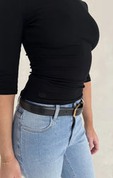 Person wearing a Renee Leather Belt Black with a gold-tone buckle over light-wash jeans and a fitted black long-sleeve top.