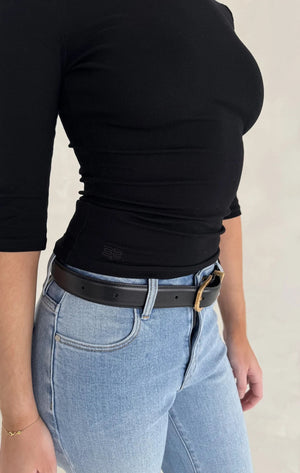 Person wearing a Renee Leather Belt Black with a gold-tone buckle over light-wash jeans and a fitted black long-sleeve top.