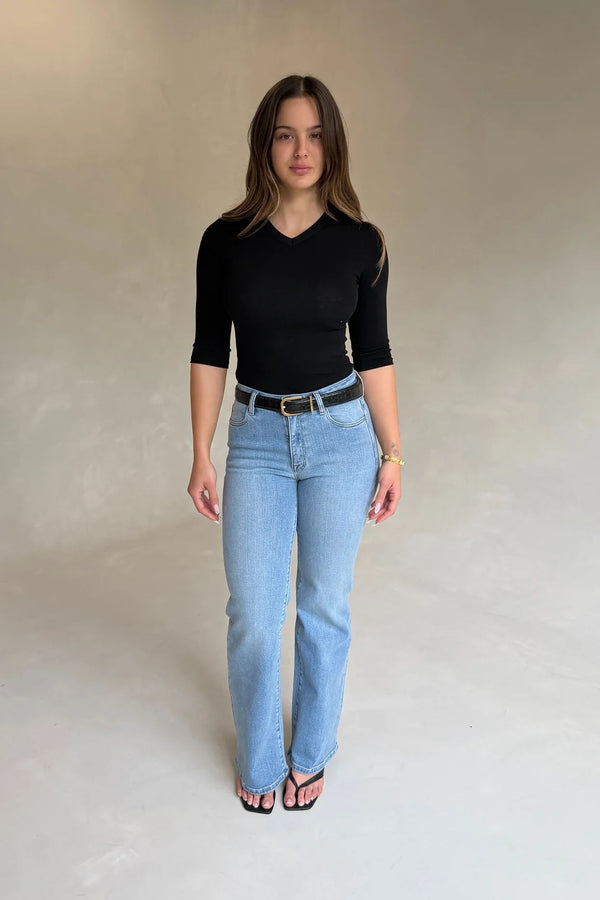 Young woman wears a Renee Leather Belt Black Croc with a black v-neck top, light-wash jeans, and black sandals against a grey backdrop.
